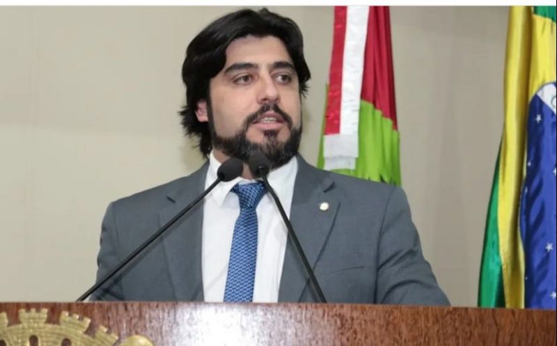 Imagem mostra vereador Maikon Costa na tribuna e a bandeira do brasil e de Santa Catarina no fundo