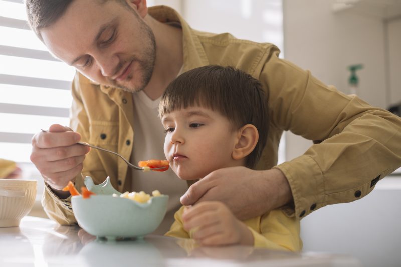 Na imagem, a foto de um homem adulto alimentando um menino 