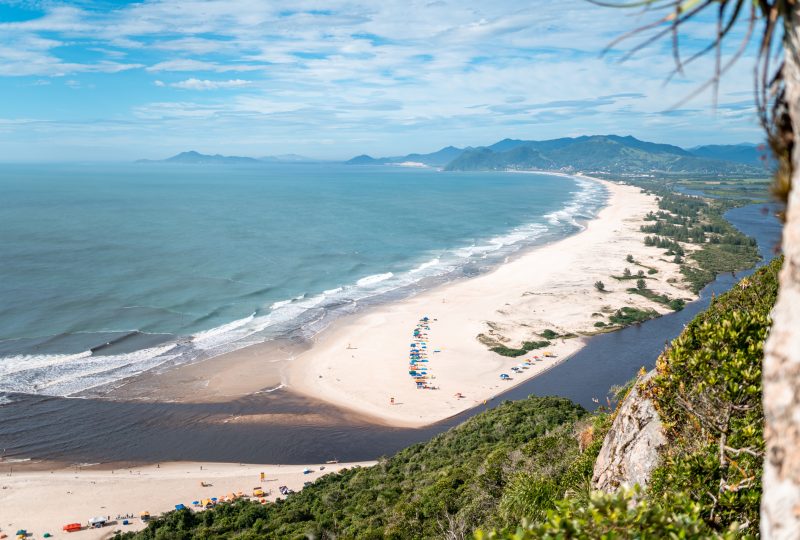 Vista aérea da Guarda do Embaú, uma praia com águas claras e vegetação em meio a rochas 