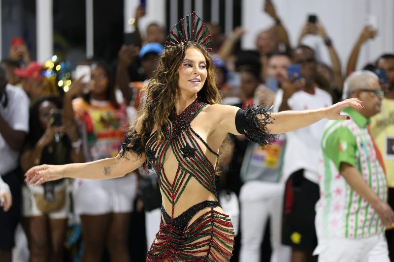 Mulher com roupa carnavalesca brilhosa nas cores verde, vermelho e preto dançando