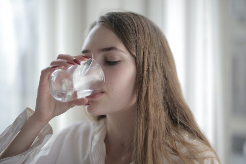 A woman drinks water from a glass cup.