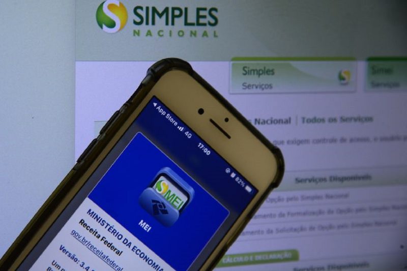 Celular com aplicativo do Simples Nacional em frente ao site do programa