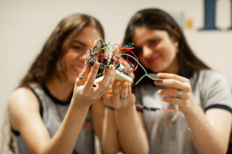 Meninas seguram nas mãos parte da estação meteorológica; o foco da solução é melhorar o trabalho dos pequenos produtores