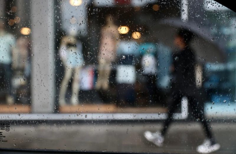 Imagem de uma pessoa na chuva com guarda-chuva olhando as vitrines de lojas 