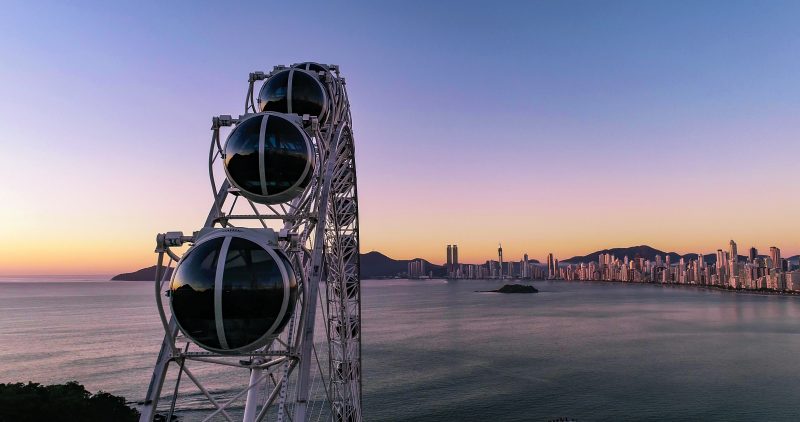 Foto de parte da Roda Gigante de Balneário Camboriú com o mar e os prédios ao fundo.