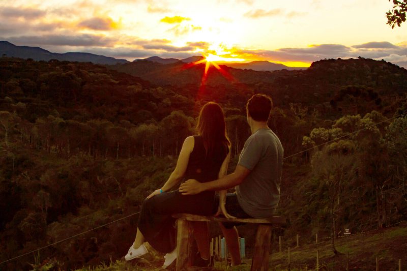 Casal de costas para a foto e admirando o sol se por atrás dos morros de Urubici.