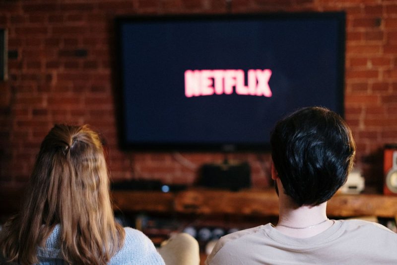 Casal assistindo ao streaming netflix com logo na tela da televisão