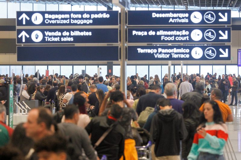 Aeroportos de SC tiveram aumento no fluxo de passageiros. Foto mostra multidão em aeroporto. Acima deles placas indicando lugares dentro do aeroporto