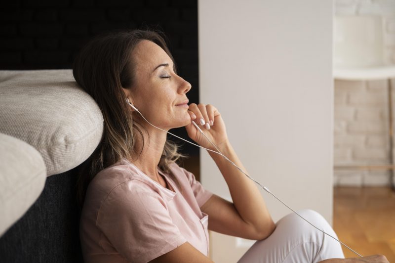 mulher sentada no chão escutando música em um fone de ouvido e com expressão de relaxamento