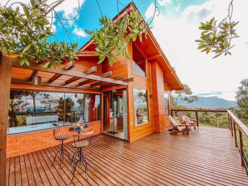 Foto de uma cabana toda em madeira com janelas e portas de vidro. Na frente dela há um grande deck de madeira e vista para a vegetação e cânions ao fundo. 