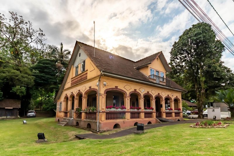 A imagem mostra a fachada a Casa Kruger, em Joinvillem com um amplo espaço verde