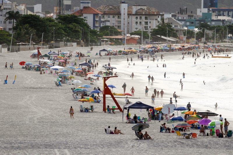 Afogamentos em praia de Florianópolis - foto mostra praia vista de longe. Banhistas aparecem com guarda-sol e cadeiras em faixa de areia da praia