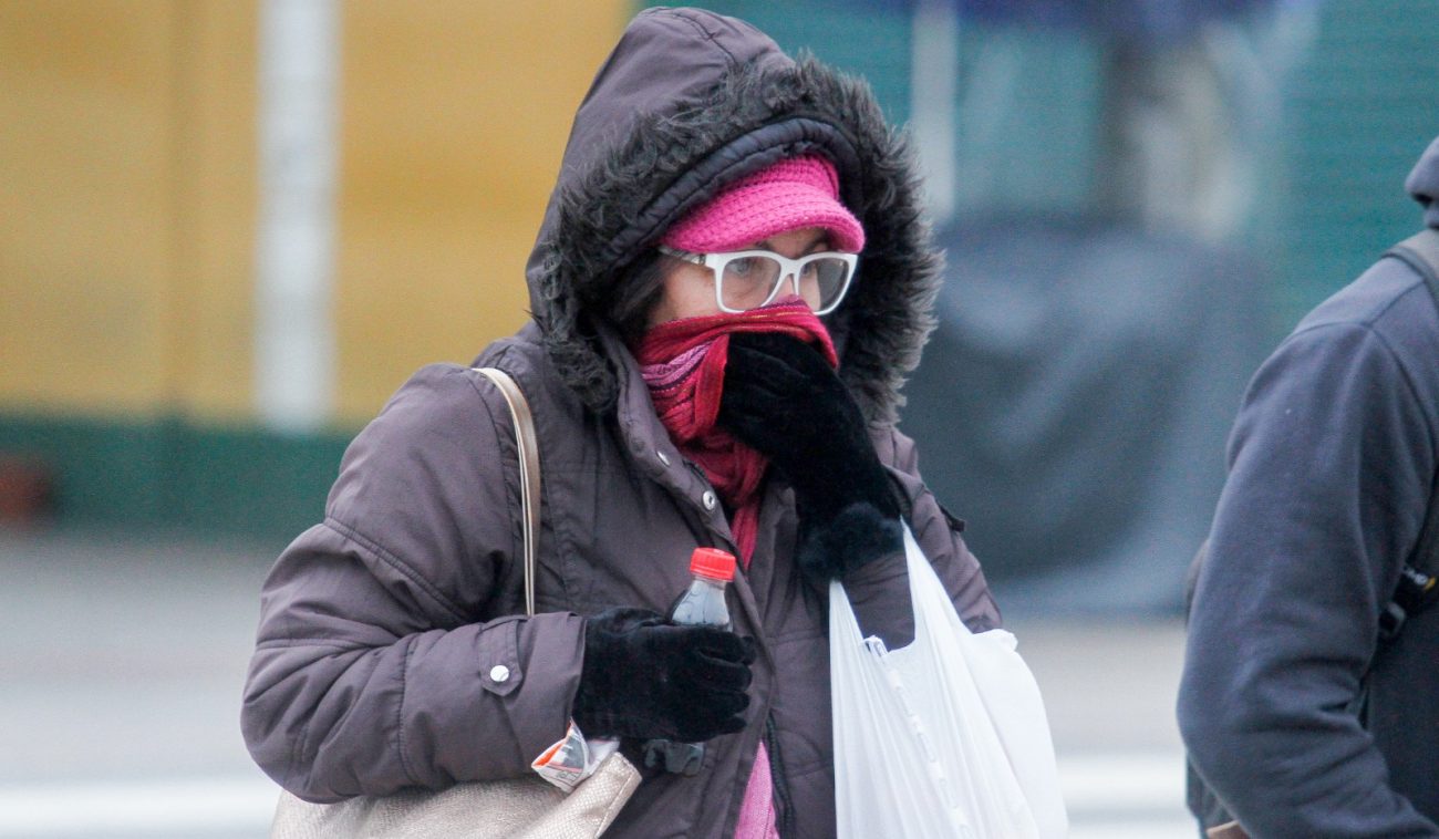 SC emite alerta laranja e prevê frio extremo, foto mostra mulher com casaco grosso preto, gorro rosa, enquanto cobre rosto com cachecol também rosa, ela usa luvas pretas e carrega uma bolsa, uma sacola e segura uma garrafa pet,