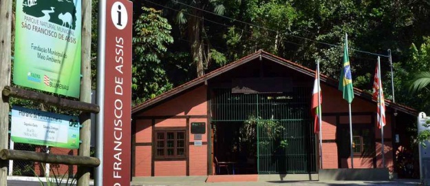 Fachada do Parque São Francisco de Assis, com uma casa de tijolos à vista de entrada e árvores ao fundo