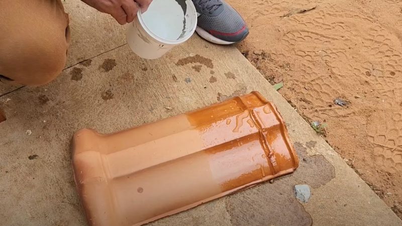Pedreiro despeja solução impermeabilizante em telha