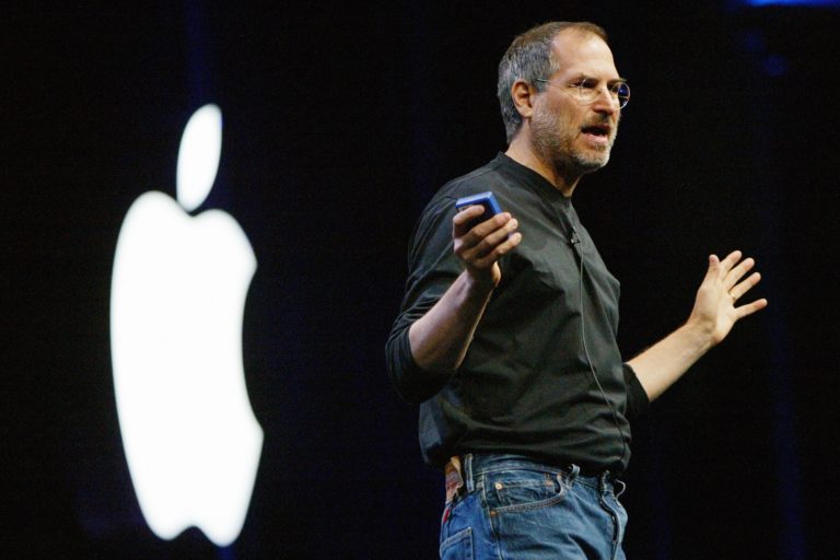 Foto mostra o Steve Jobs com a logo da Apple no fundo