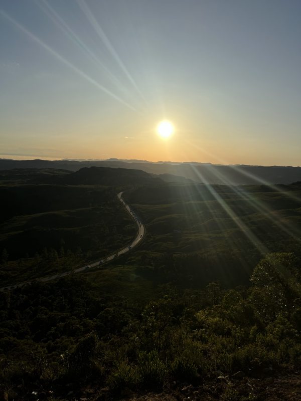 Foto mostra o nascer do sol do alto do Morro da Boa Vista, em Rancho Queimado. Mais escuro na foto aparecem morros verdes cortados pela BR-282. 