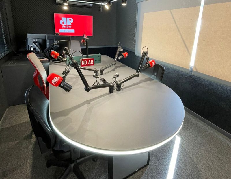 estúdio da emissora de rádio Jovem Pan Chapecó com mesa, cadeiras, microfones e mesa de áudio, onde são gravados os episódios do Business cast