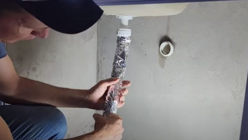 Pedreiro enrosca papel alumínio em tubo do sifão
