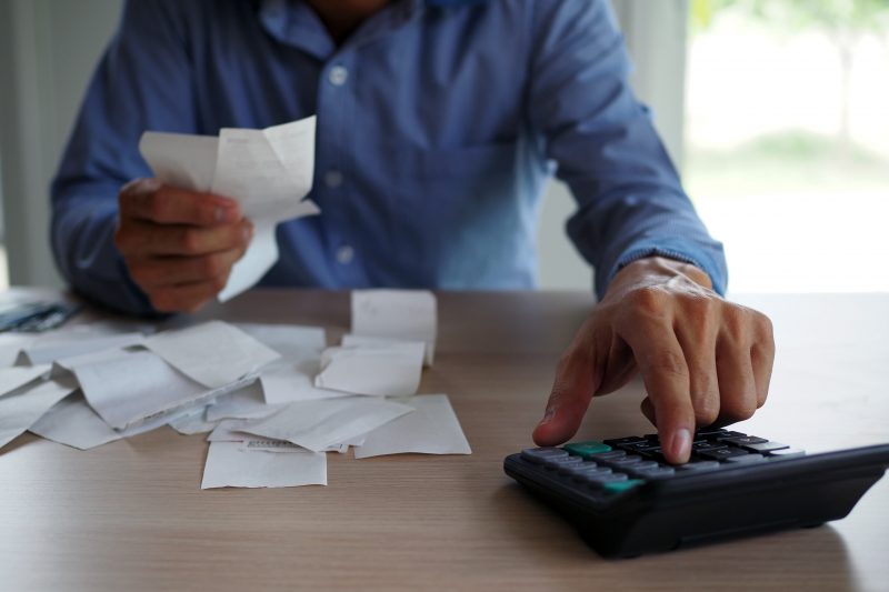 Na imagem, um homem fazendo cálculos com uma calculadora e alguns papéis na mesa, para ilustrar as vendas de micro e pequenos negócios