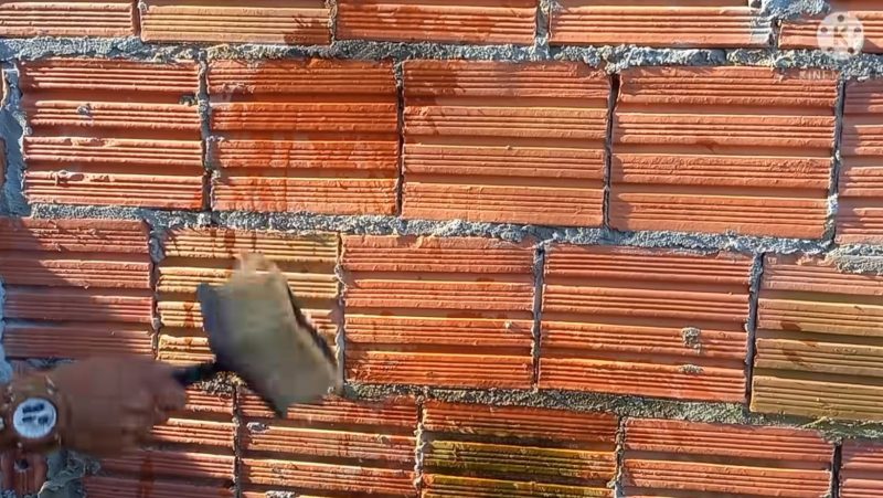 Pedreiro molha parede de tijolo para garantir fixação da massa que virá a seguir