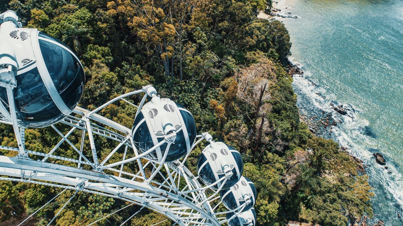 À esquerda da foto aparece parte da roda gigante de Balneário Camboriú. Abaixo e ao fundo, aparece um morro verde e uma pequena parte do mar. 