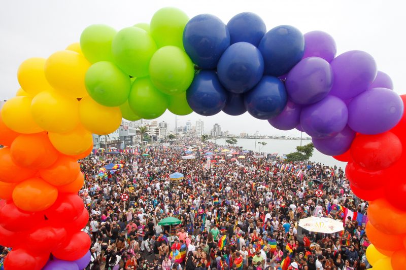 Parada LGBTI+ de Florianópolis, foto mostra arco de balões nas cores do arco-íris com multidão atrás