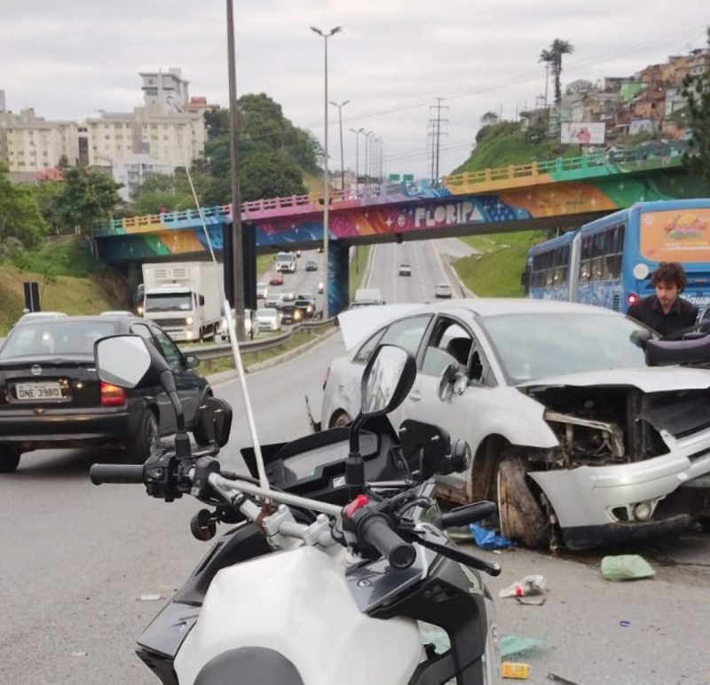 Carro completamente destruído após bater na mureta de proteção central da Via Expressa, aparece uma moto e um carro preto na foto
