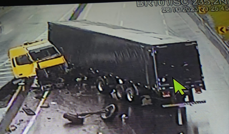 Carreta destruída tombada em uma estrada. Na foto, é possível ver pneus soltos e a cabine amarela do veículo desconectada do compartimento de carga. 