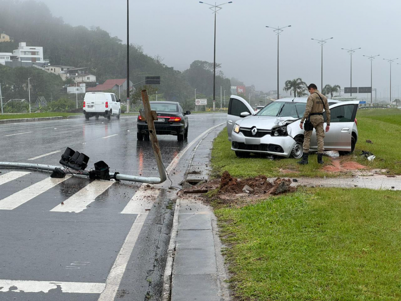 Carro destroçado após um acidente. Na foto é possível ver um semáforo caído no chão e um policial militar em frente ao veículo danificado