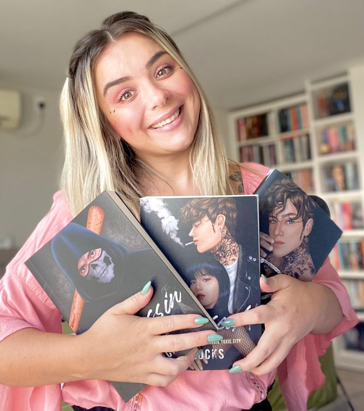Francine Locks sorri para foto com seus livros de Dark Romance na mão