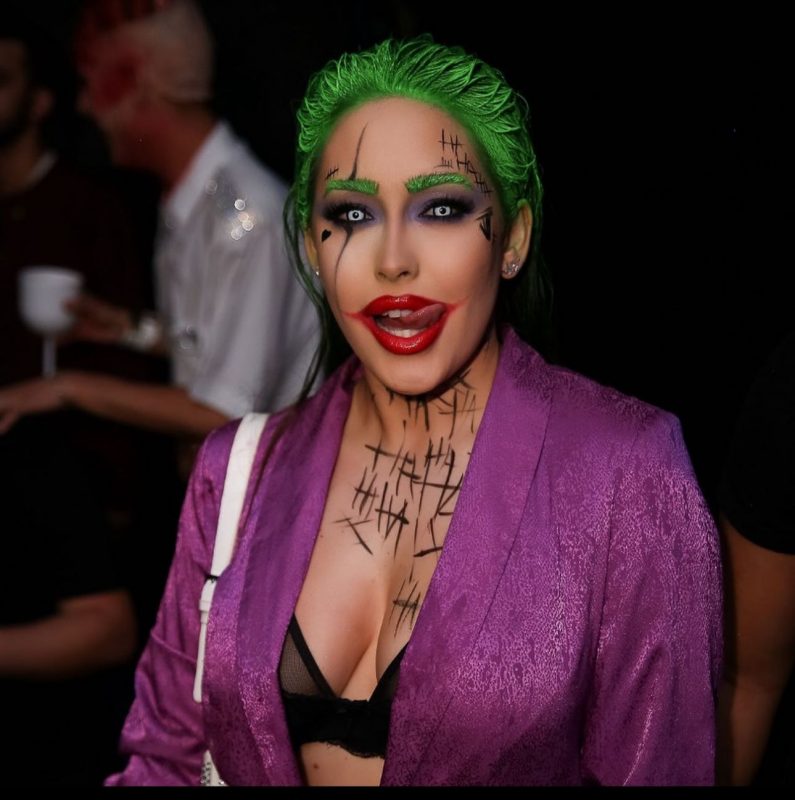 Mulher fantasiada do personagem "Coringa" faz careta para foto de divulgação de festa de Halloween