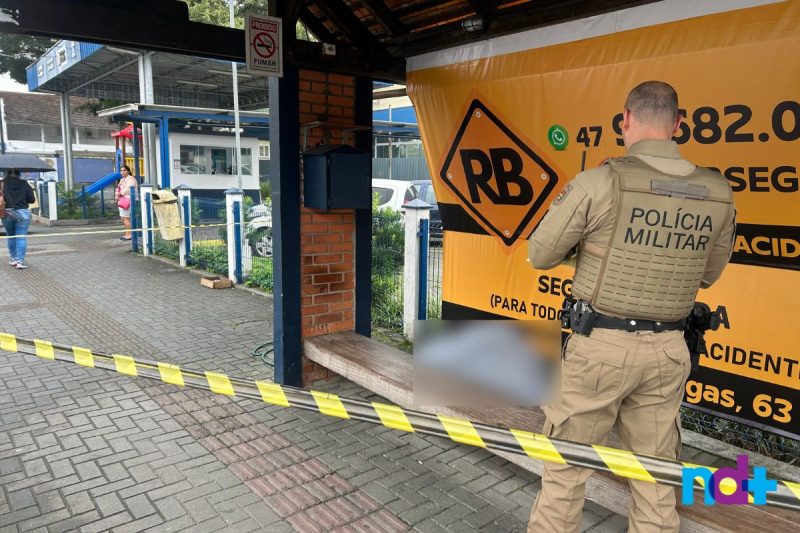 Área do ponto de táxi, em Joinville, isolada. Ao fundo, o corpo do homem foi borrado. À frente, está o Polícia Militar