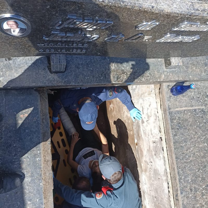 Uma mulher está dentro de um túmulo junto com dois bombeiros que a socorrem