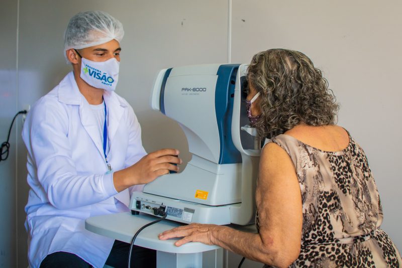 Mulher idosa fazendo exame de visão com ajuda de um profissional. Ele usa uma máscara de prevenção ao coronavírus.