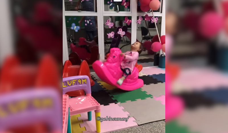 Menina brincando e se divertindo balançando em um cavalo rosa de brinquedo