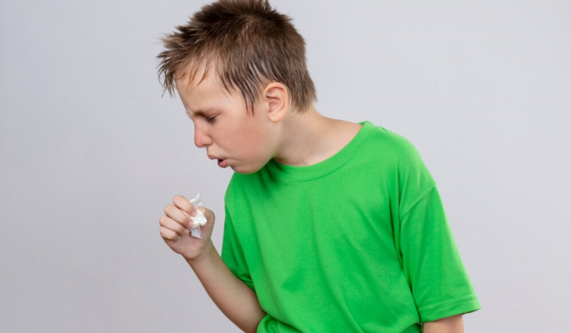 Menino branco usando camiseta verde neon tossindo em lenço de papel