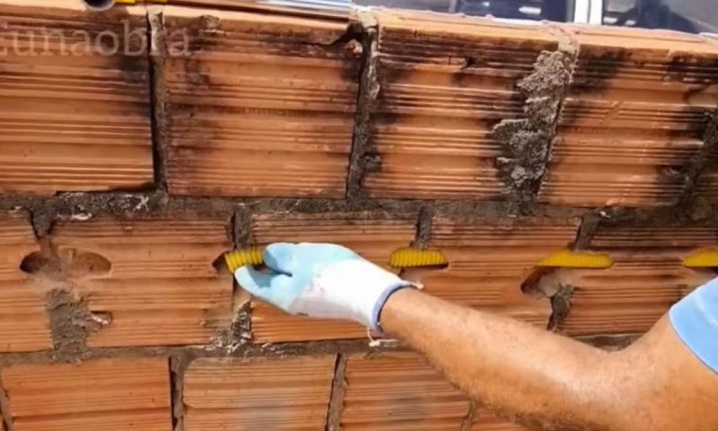Pedreiro instala conduíte em buraco feito na parede de tijolos