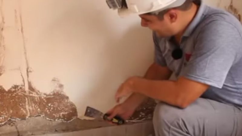 Pedreiro descasca rodapé de parede com umidade para ensinar técnica