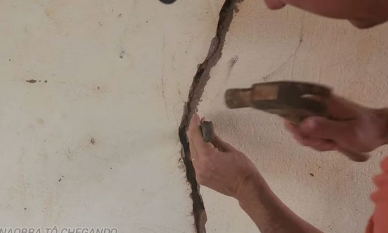Pedreiro martelando parede onde há uma enorme rachadura