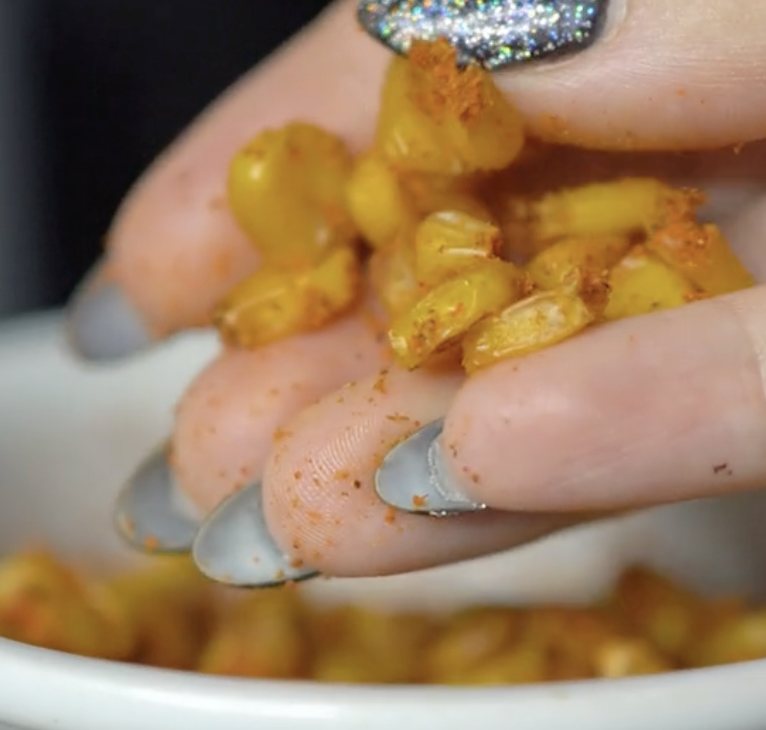 Resultado do salgadinho de milho. É possível ver que ele está bem temperado. A mão de uma mulher segura o milho.