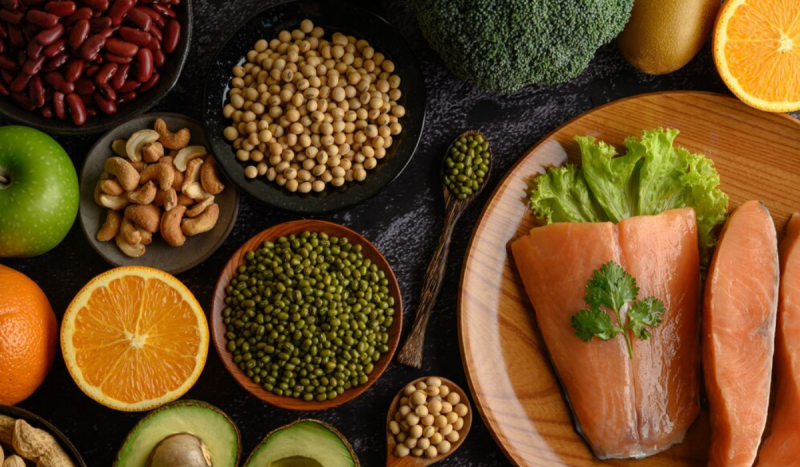 Photo of food from above, in the photo there are beans, chestnuts, oranges, peas, salmon, avocado, green apple and broccoli, arranged in round containers.