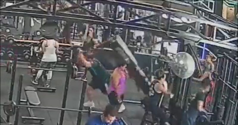 Frame mostra o homem puxando o aparelho na academia e o mesmo caindo em cima dele