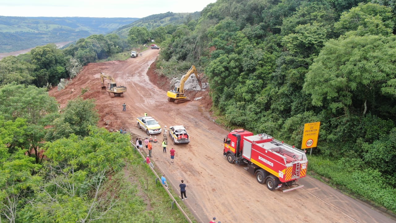 Na foto é possível ver uma rodovia coberta de terra com caminhões e veículos de forças de segurança avaliando o terreno.