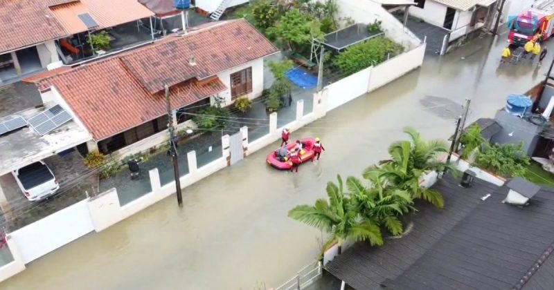 Imagem aérea feita por drone mostra bairro Gravatá de Navegantes coberto por água, é possível ver também equipe do Corpo de Bombeiros resgatando idoso