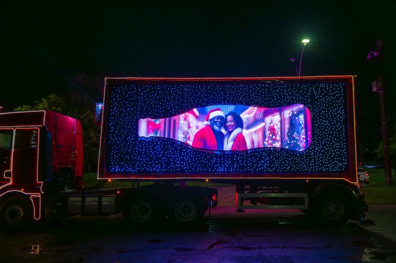 Caminhão da caravana iluminada da Coca-Cola com ativação passando em uma rua