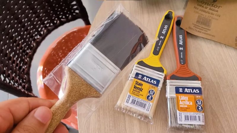 Diferentes tipos de pincel espalhados em cima da mesa enquanto pintor segura um deles, de cerda preta