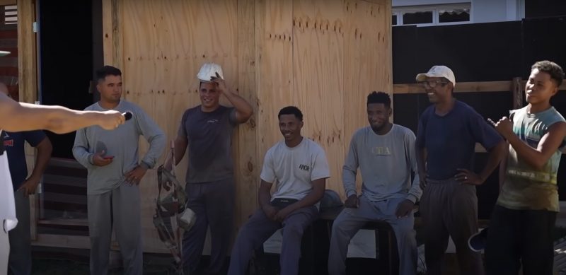 Seis pedreiros na obra estão sorrindo enquanto são entrevistados