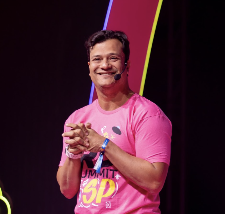 CEO da RD Station sorrindo com as mãos cruzadas em um palco luminoso; ele falou sobre inteligência artificial