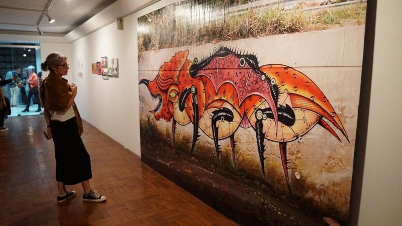Na foto uma mulher contempla uma reprodução em grande escala da obra do artista Paulo Noia na exposição "Jardim das Delicias Bestiais"